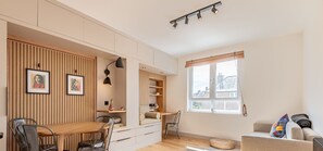 Une pièce moderne avec un mur lambrissé en bois, un coin repas, un espace salon avec un canapé et un fauteuil, et une fenêtre offrant une vue agréable.