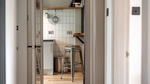 A narrow hallway leading to a kitchen with white cabinets, a hanging pot rack, and a stool. - Boase Avenue (No 69) | St Andrews (St Andrews)