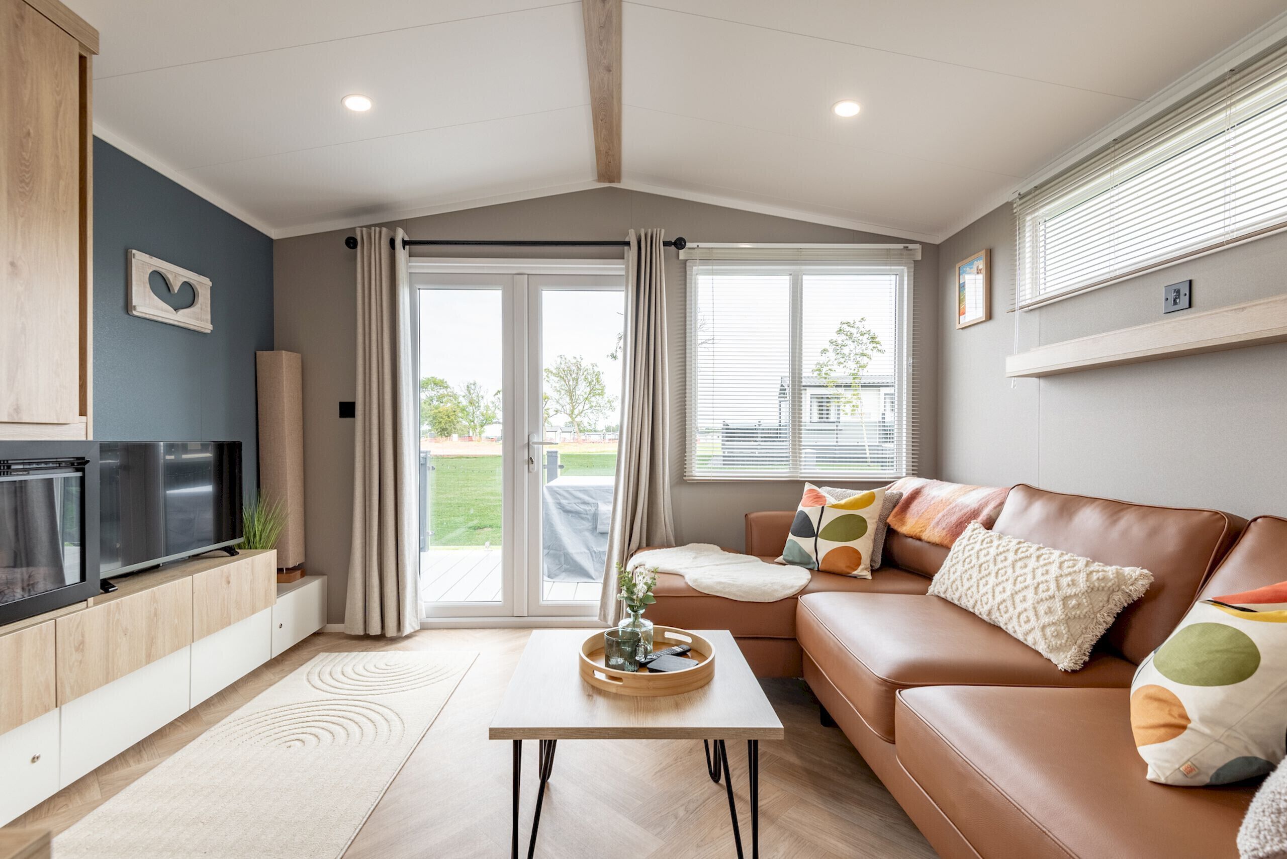 A modern living room with a brown leather sofa, a flat-screen TV, and a sliding glass door leading to a balcony.