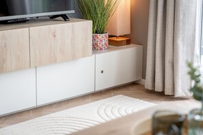 A modern living room with a wooden cabinet, a television, a decorative plant, and a beige curtain. - Lodge No 83 | Hot Tub | Stewart's Resort Cameron (Cameron)