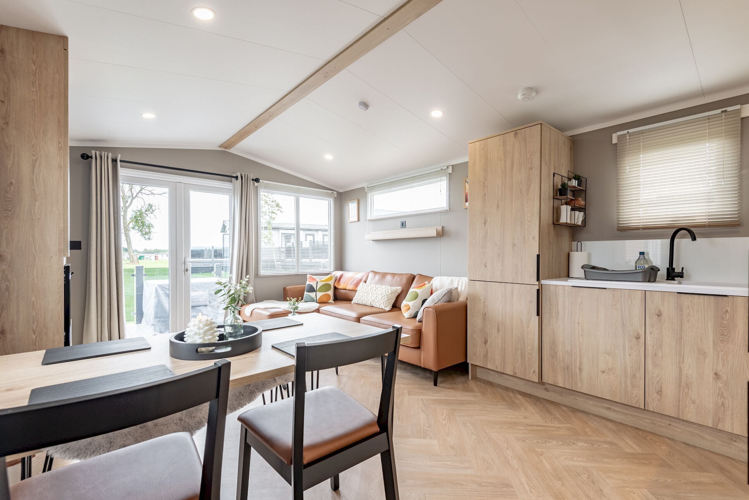 Eine moderne Küche mit Holzausstattung, ein Essbereich mit Tisch und Stühlen sowie eine Sitzecke mit einer Couch.