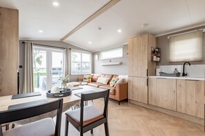 A modern kitchen with wooden cabinets, a dining area with a table and chairs, and a sofa. - Lodge No 83 | Hot Tub | Stewart's Resort Cameron (Cameron)