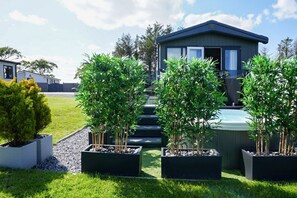 A modern building with a dark exterior, a set of stairs leading to a door, and a well-maintained garden with several potted plants. - Lodge No 83 | Hot Tub | Stewart's Resort Cameron (Cameron)