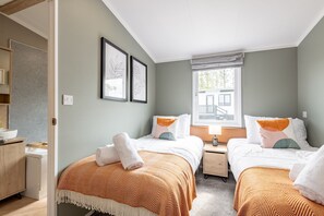 A bedroom with two beds, a window with a view, and a bedside table with a lamp. - Lodge No 83 | Hot Tub | Stewart's Resort Cameron (Cameron)