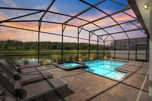 Piscina exterior cubierta con sillas de descanso y jacuzzis, rodeada por una estructura metálica y con vistas a un lago.