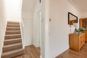 Un escalier menant à une porte, un meuble en bois avec un miroir, et une plante posée sur le dessus.