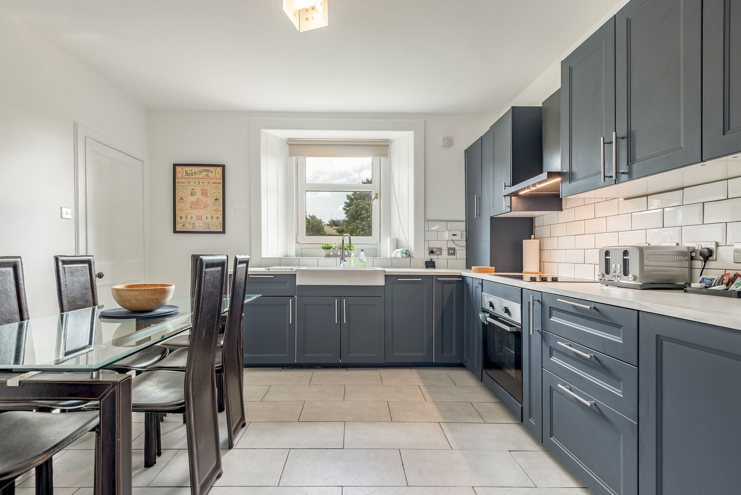 A modern kitchen with dark cabinets, a glass dining table, and a window providing natural light.