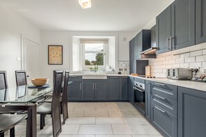 Une cuisine moderne avec des meubles de couleur sombre, une table à manger en verre et une fenêtre qui laisse entrer la lumière naturelle.
