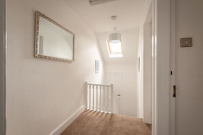 A hallway with a white door, a white railing, and a mirror on the wall.