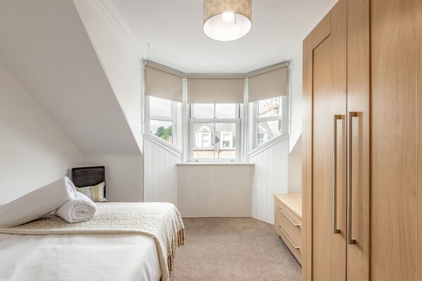 A bedroom with a bed, a window, a wardrobe, and a radiator.