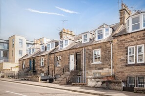 Una hilera de casas urbanas de piedra con arquitectura uniforme, con pequeños jardines delanteros y una calle despejada al frente.