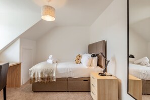 A modern bedroom with a bed, bedside table, lamp, and a large mirror. - Kinness Place (No 6) (St Andrews)