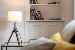 Une pièce avec une table en verre, une lampe, une bibliothèque et un lit avec des oreillers.