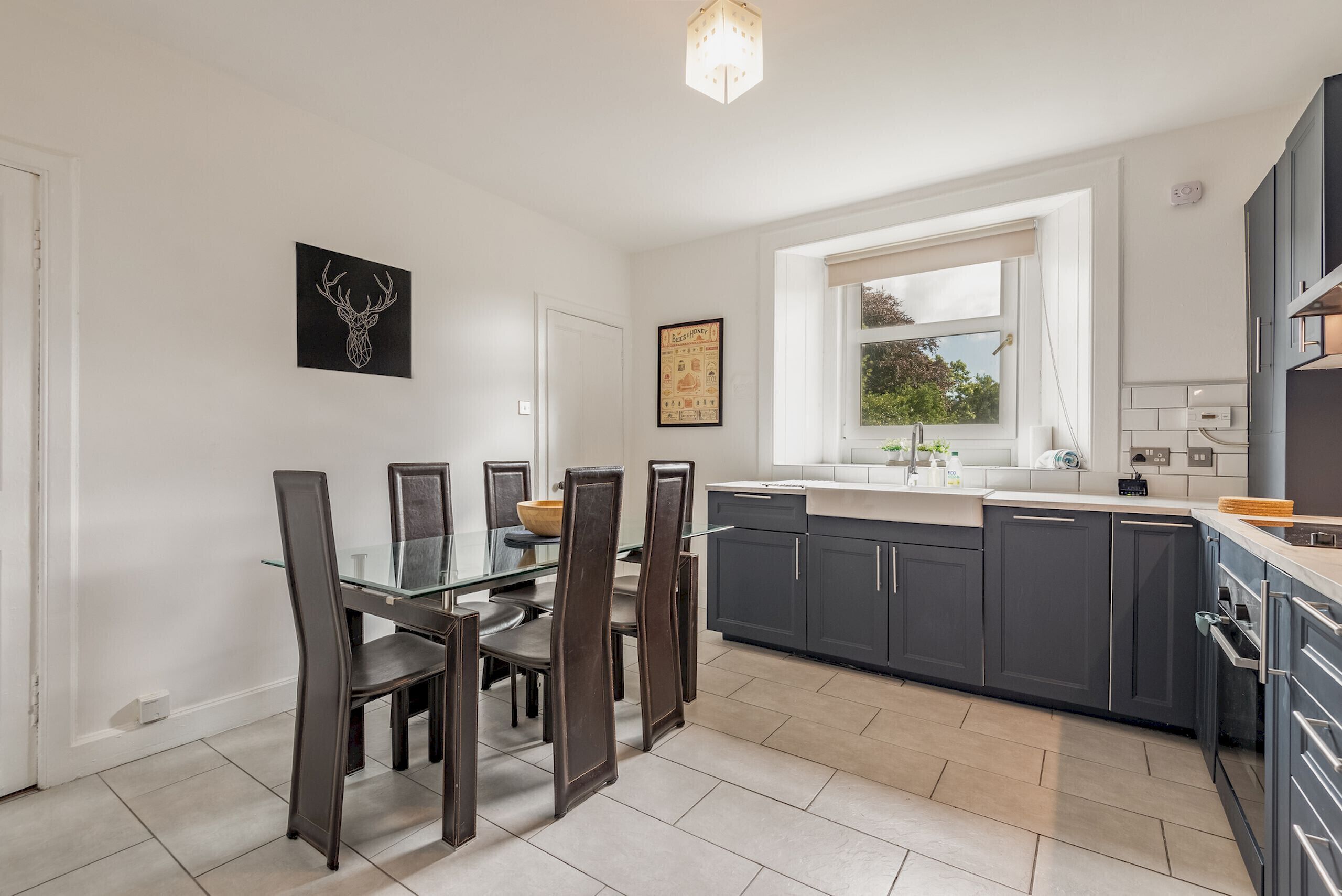 A modern kitchen with dark cabinets, a glass dining table, and a window providing natural light.