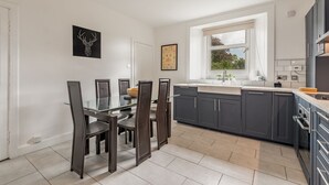 A modern kitchen with dark cabinets, a glass dining table, and a window providing natural light. - Kinness Place (No 6) (St Andrews)