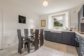 A modern kitchen with dark cabinets, a glass dining table, and a window providing natural light.