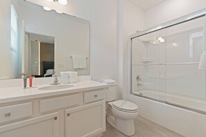 A modern bathroom with a white vanity, a toilet, and a glass-enclosed shower. - 12BR house with private pool in Bella Vida (Kissimmee)