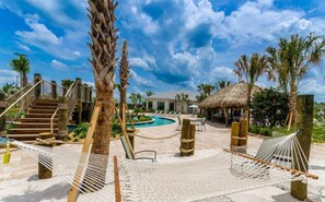 Un área de piscina en un resort con una construcción de techo de paja, palmeras y hamacas.
