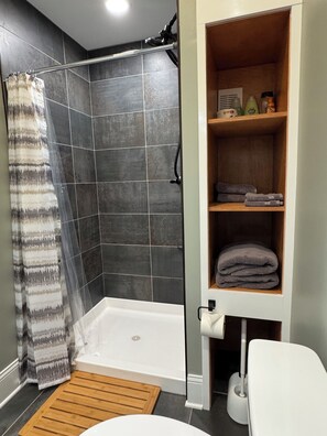 A bathroom with a shower, toilet, and a shelf with towels.