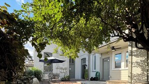 A courtyard with a stone bench, a table, and chairs under a tree. There is a building with a white facade and a door visible. - Stadium Stay #4  The Presidents Suite.  Free Parking.  (Indianapolis)
