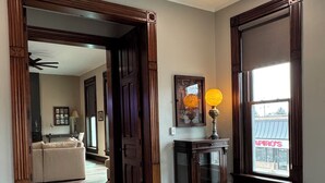 A spacious hallway with wooden flooring, a large window with a view of a building, and a door leading to another room. - Stadium Stay #4  The Presidents Suite.  Free Parking.  (Indianapolis)