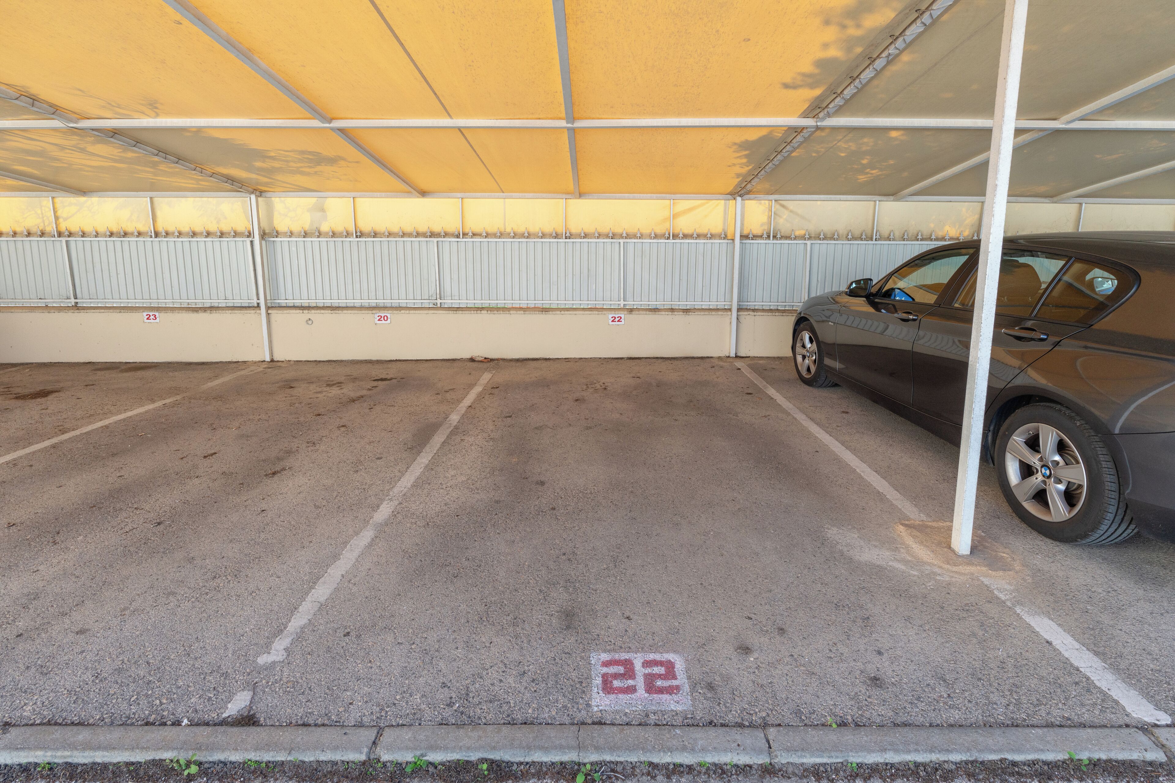 A parking area with marked spaces, a car parked, and a yellow canopy overhead.