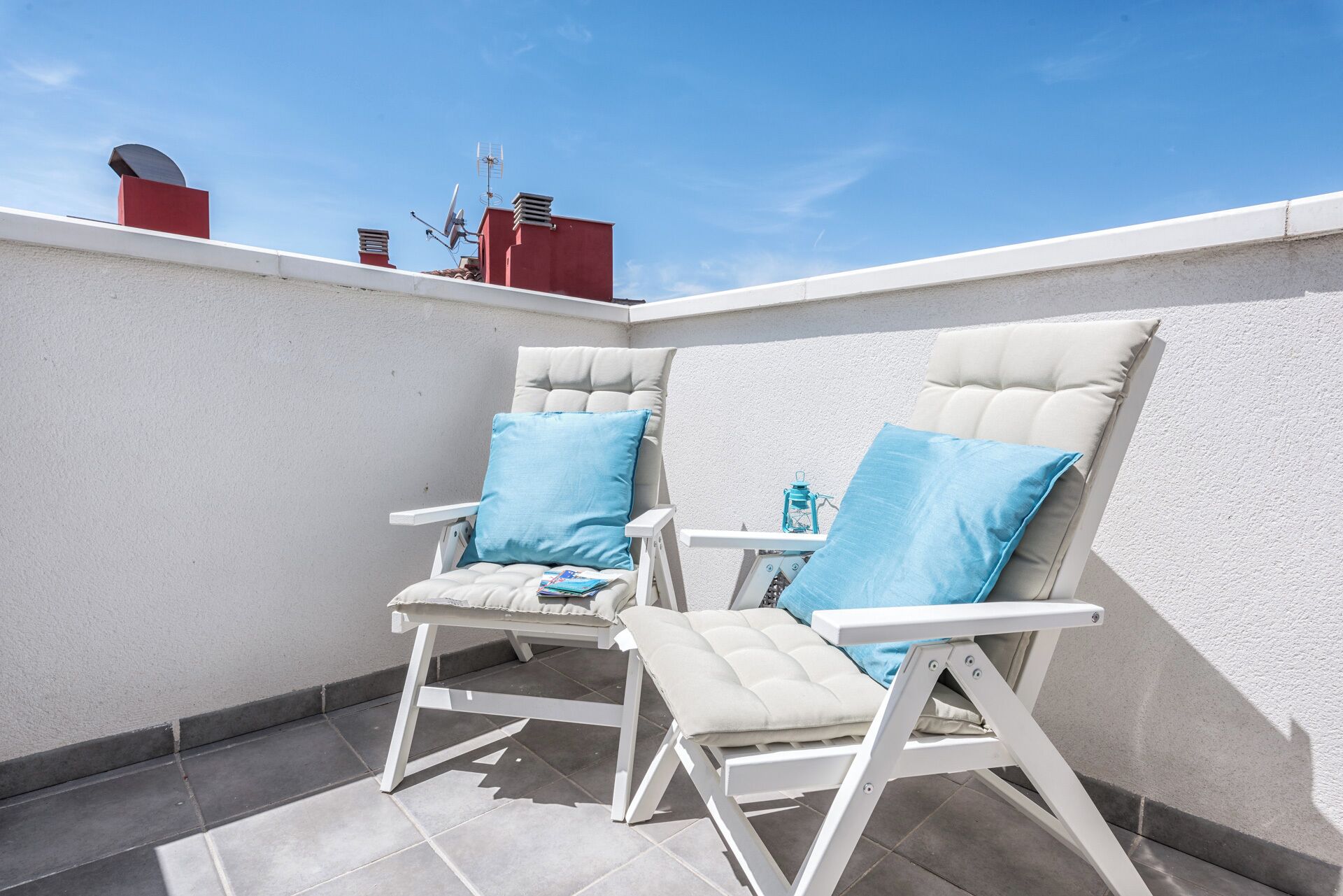 Two white lounge chairs with blue cushions on a tiled patio.