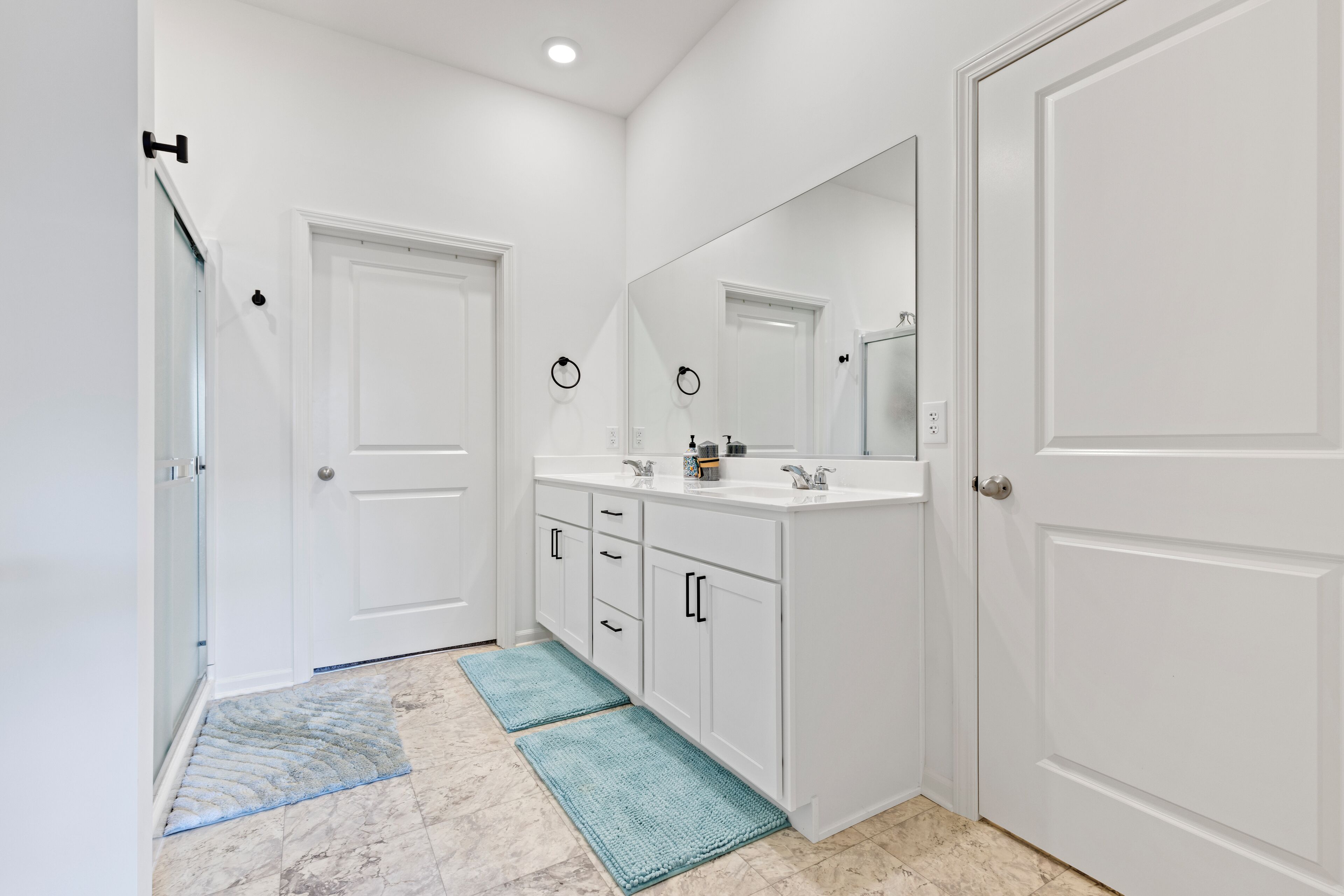 A bathroom with white cabinets, a large mirror, and a door with a towel ring.