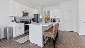 A modern kitchen with white cabinetry, stainless steel appliances, and a central island with bar stools. - Wonder Lake Elegance: Serene 2BR Townhome Retreat (Wonder Lake)