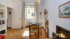 Een eetgedeelte met een tafel voor vier personen, een boekenkast, een radiator en een schilderij aan de muur.
