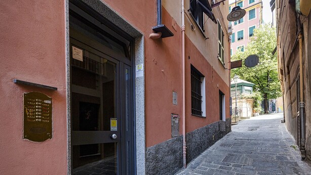 Een smalle, geplaveide straat met een gebouw dat een grote glazen deur en een metalen plaquette aan de gevel heeft.