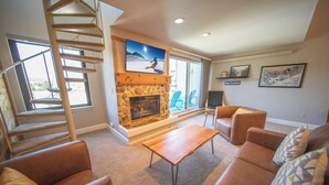 A living room with a stone fireplace, a wooden coffee table, leather sofas, and a spiral staircase.