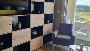 Una sala de estar moderna con televisor empotrado, estanterías de madera y negras, un sillón gris y una pequeña mesa con una planta en maceta.