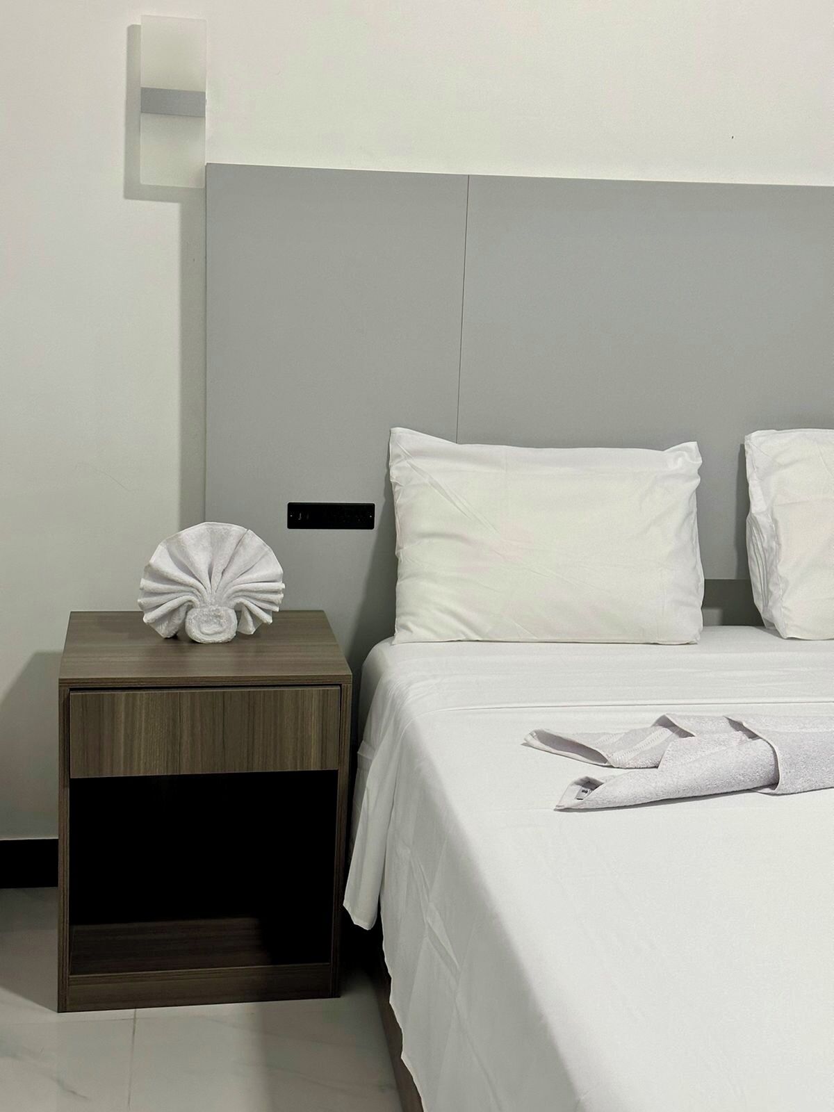 Een hotelkamer met een bed, nachtkastje en een wandlamp.