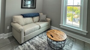 Un salon moderne avec un ventilateur de plafond, une grande fenêtre offrant une belle vue, un canapé gris et une table basse ronde.