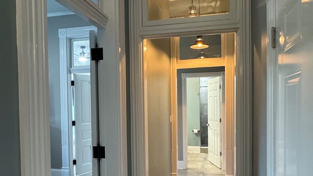 Un couloir doté d’un plancher en bois, de murs blancs et d’un luminaire au plafond.