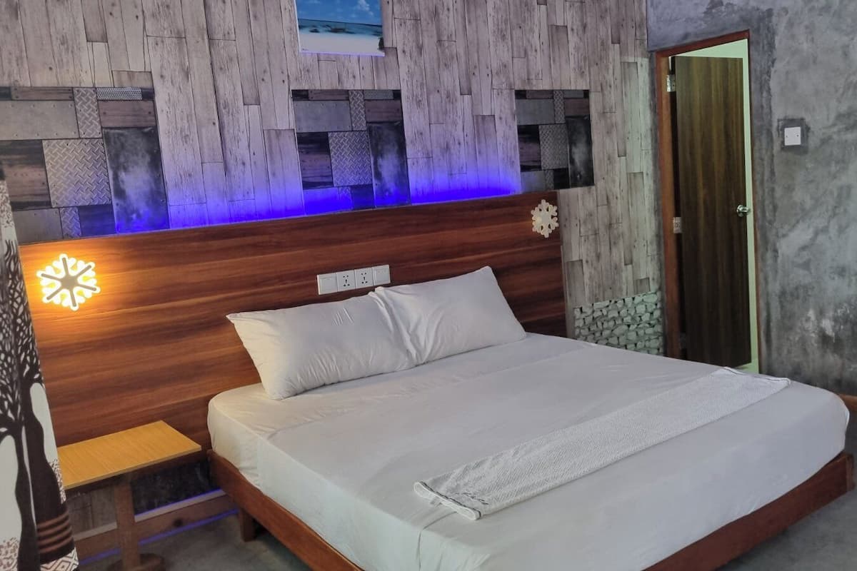 Een slaapkamer met een houten hoofdbord, een bed met witte lakens, een nachtkastje en een wandlamp.