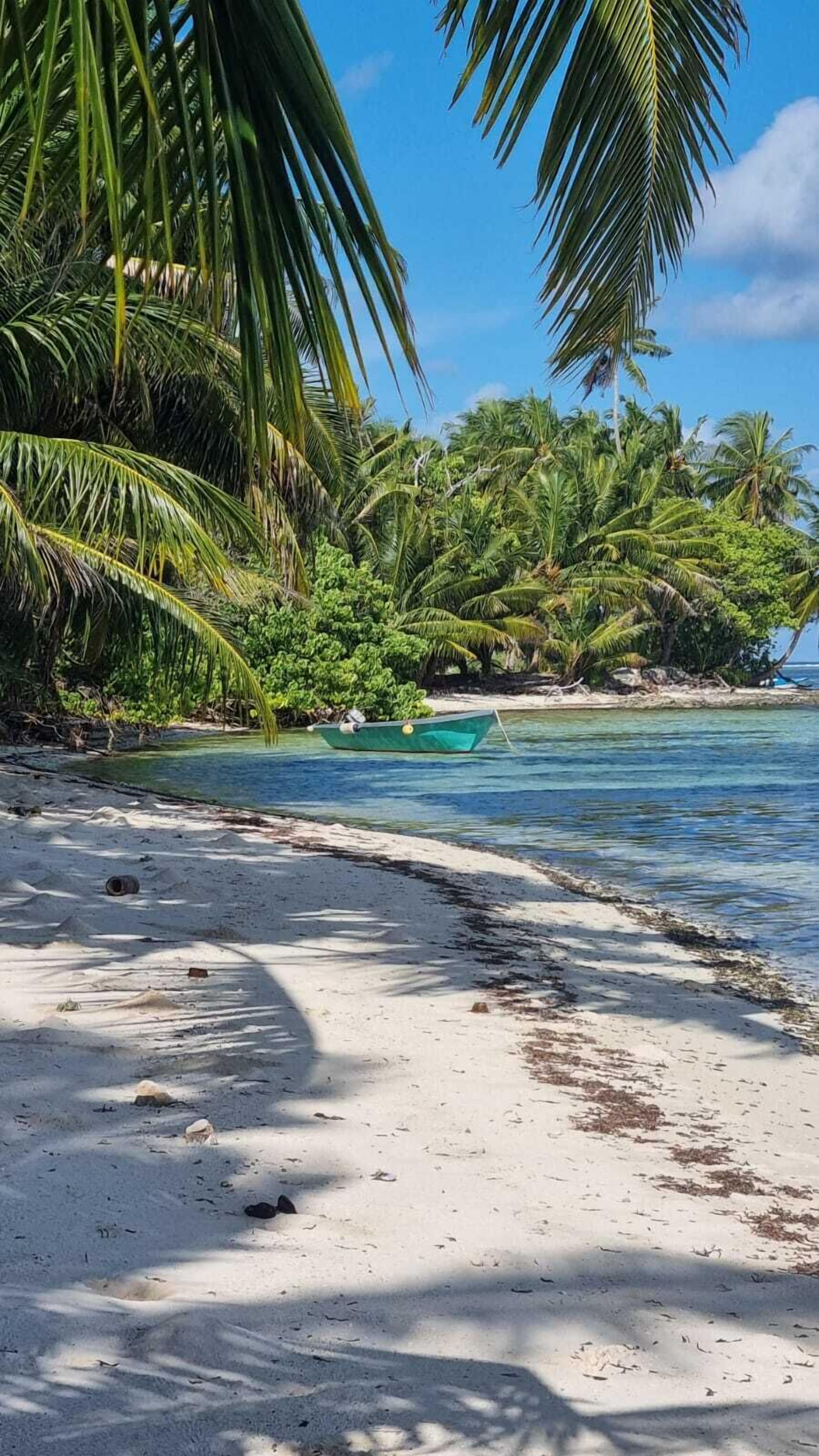 A beach with white sand, clear turquoise water, and a small green boat anchored near the shore.