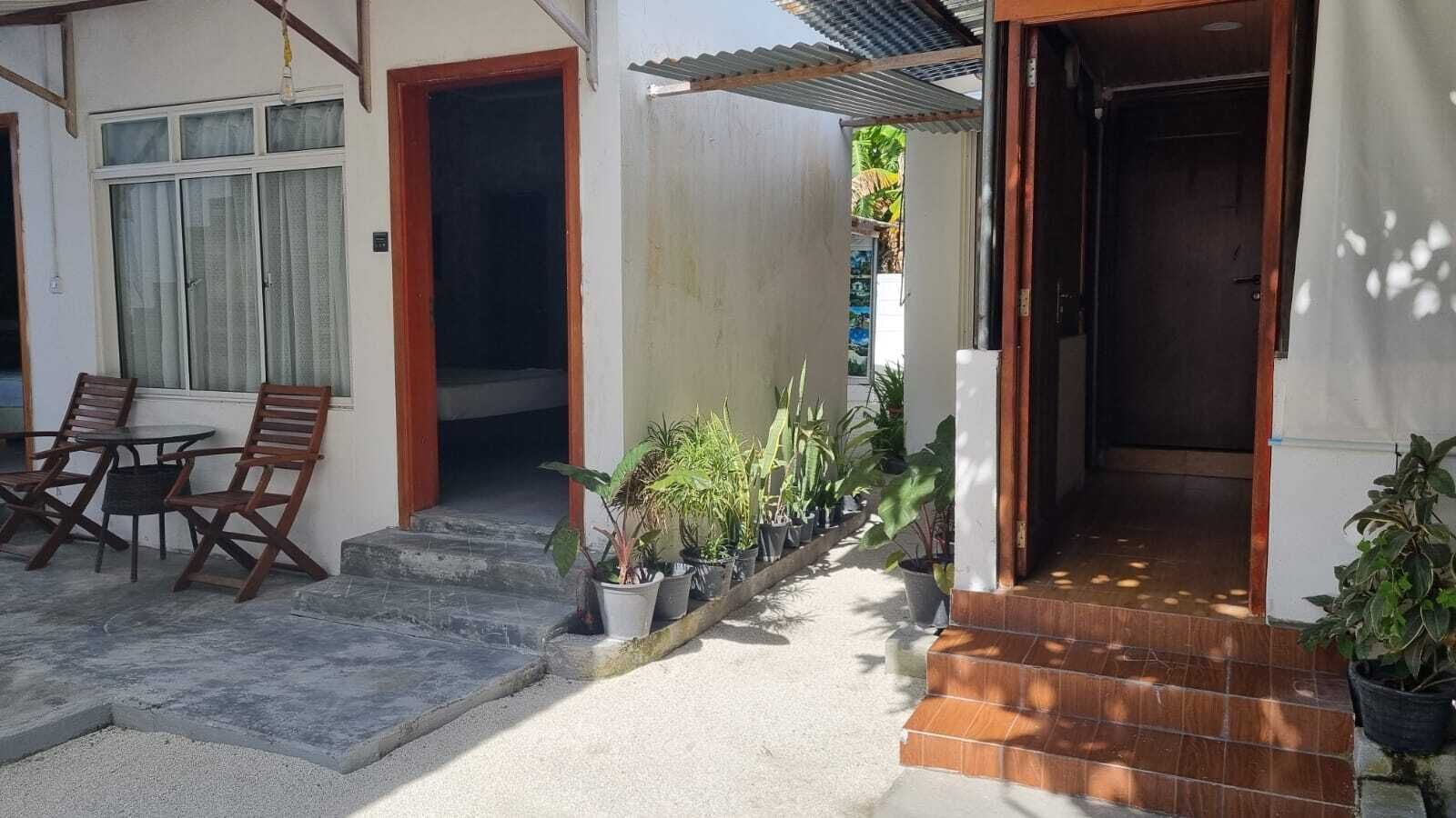 Una casa con un patio attrezzato con tavolo e sedie, una scala che conduce all'ingresso e piante in vaso lungo il vialetto.
