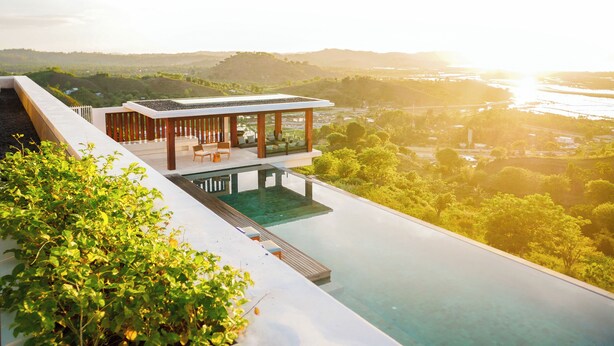 Une piscine à débordement moderne, dotée d’un fond en verre, qui offre une vue imprenable sur un paysage luxuriant et sur les contours d’une ville lointaine.