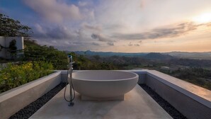 Une grande baignoire autoportante installée sur une terrasse sur le toit, offrant une vue sur un paysage montagneux.