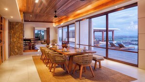 Un espace repas moderne avec une table en bois, des chaises en osier et une vue sur le paysage grâce à de grandes fenêtres.