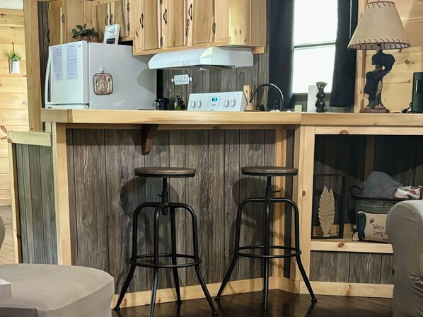 A kitchen with wooden cabinets, a white refrigerator, a stove, two stools, and a window with natural light.