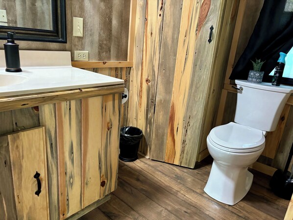 Un baño con diseño rústico de madera, que incluye un lavamanos con grifo negro, un inodoro y un cubo de basura negro.