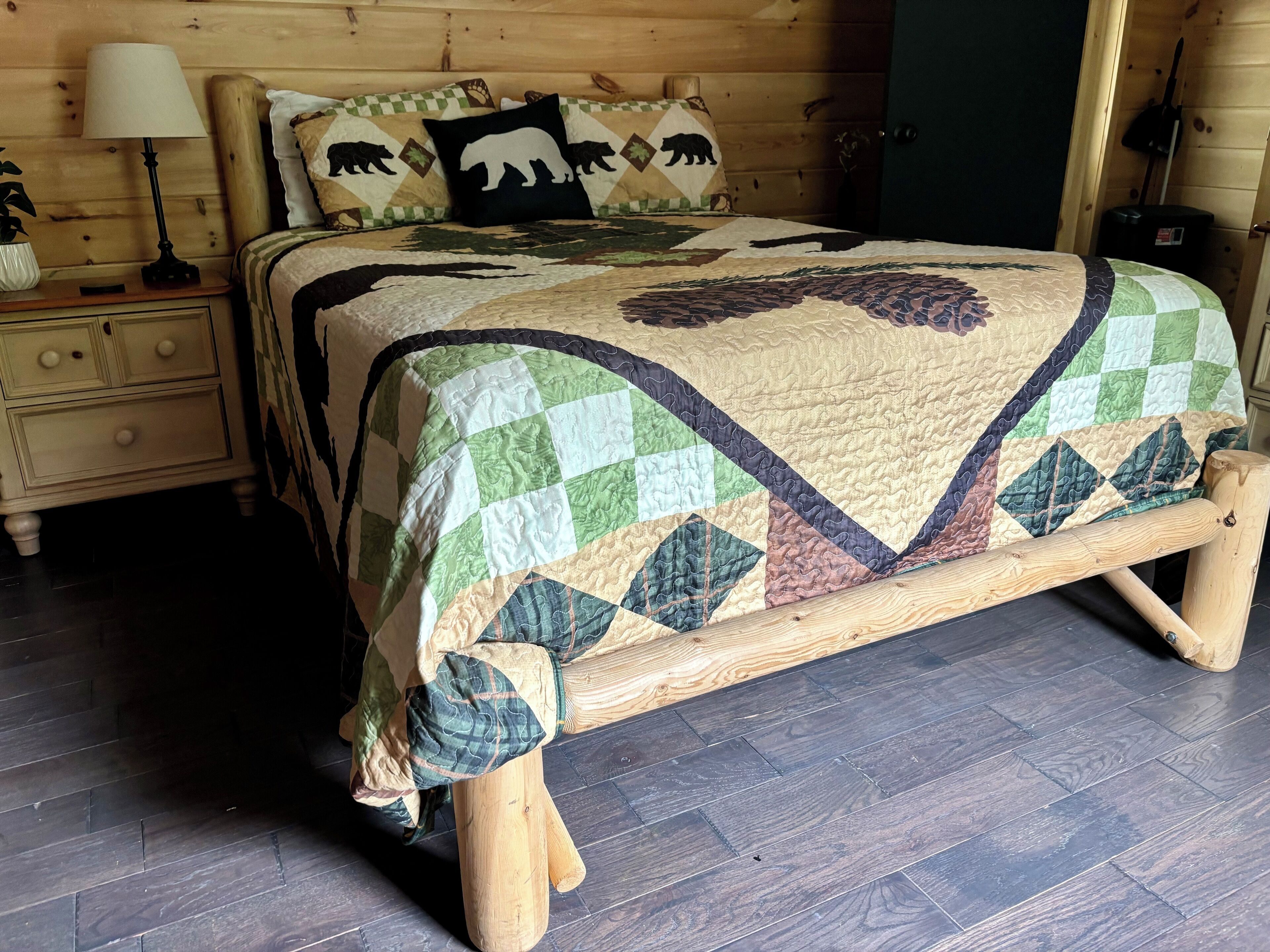 A wooden bed with a quilt featuring a bear pattern, a bedside table with a lamp, and a nightstand with drawers.