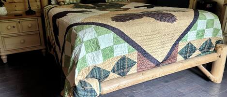 A wooden bed with a quilt featuring a bear pattern, a bedside table with a lamp, and a nightstand with drawers.