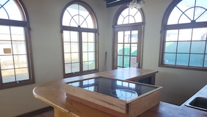 A kitchen with a wooden countertop and a glass-top island. There are three arched windows providing natural light. - Sunflower Room Apartment (Hobbs)