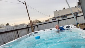 A hot tub with a wooden deck in a backyard. - Sunflower Room Apartment (Hobbs)