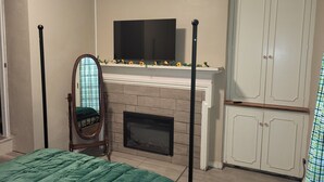 A bedroom with a bed, a fireplace, a TV mounted above it, and a wardrobe. - Sunflower Room Apartment (Hobbs)