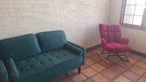 A room with a white brick wall, a teal sofa, and a pink rocking chair. - Sunflower Room Apartment (Hobbs)